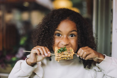 Portrait of hungry with curly hair eating corn at restaurant