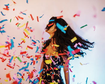 Colorful confetti against young woman standing by wall