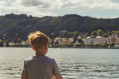 Rear view of boy looking at river against sky