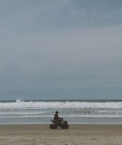 Young woman riding vehicle at beach against sky