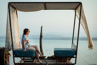 Woman sitting on chair by sea against sky