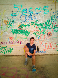 Full length of man sitting against graffiti wall