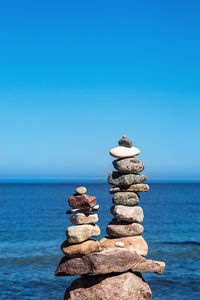 Stack of stones by sea against blue sky