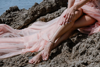 Low section of woman sitting on rock by sea