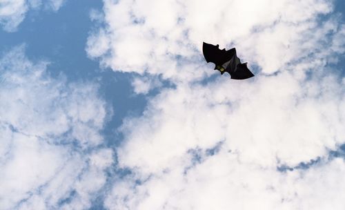 Low angle view of black kite flying against cloudy sky