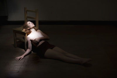 Thoughtful shirtless woman lying down in darkroom