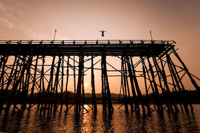 Low angle view of silhouette man jumping in lake during sunset