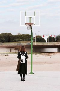 Man standing on basketball hoop against sky