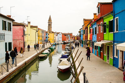 People on canal amidst buildings in city against sky