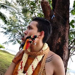 Close-up of young man with pierced mouth standing against tree trunk