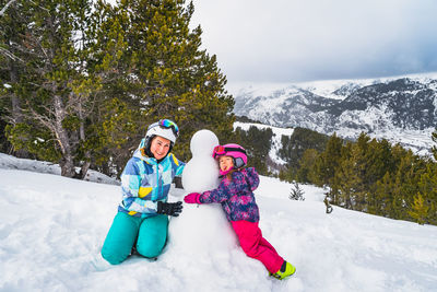 Mother and daughter hugging snowman. ski winter holidays in andorra