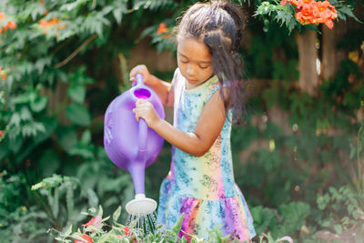 Diverse mixed race pre school girl outdoors during summer watering plants in garden