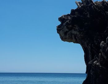 Rock formation by sea against blue sky