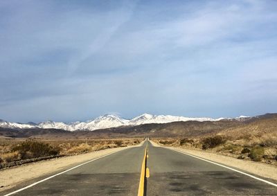 Empty road by mountains against sky