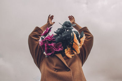 Person face covered with bouquet against sky