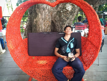 Portrait of man sitting on red heart shape seat at outdoor cafe