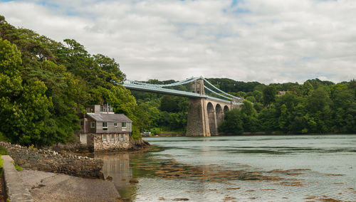 Menai bridge over river against cloudy sky