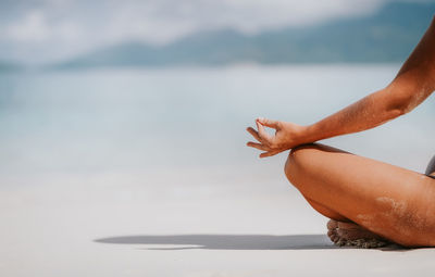 Low section of woman meditating at beach
