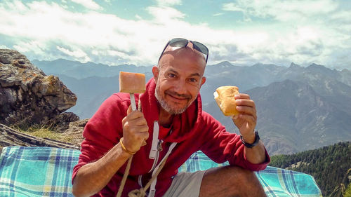 Portrait of man holding ice cream against mountains