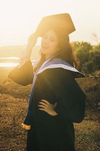 Portrait of young woman in graduation gown standing on field