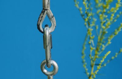 Low angle view of metallic chain against blue sky