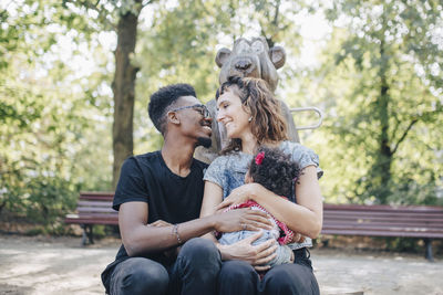 Smiling mother and father looking at each other while sitting with daughter in playground