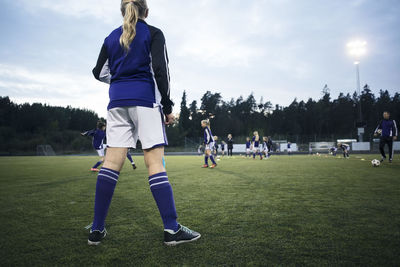 Rear view of girl looking at players playing on soccer field