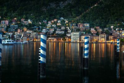 Boats moored in river by illuminated buildings in city