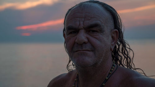 Close-up portrait of mature man against sea during sunset