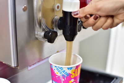 Close-up of hand using ice cream machine while filling cup at shop