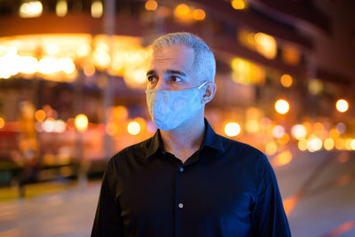 Portrait of man standing against illuminated city at night