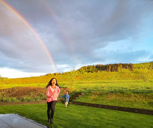 Woman standing on field against rainbow in sky