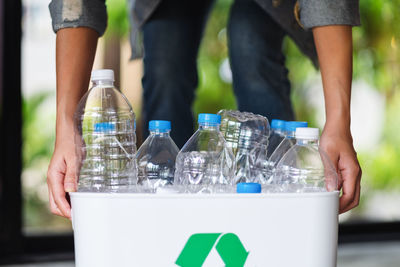 A woman collecting and holding recyclable garbage plastic bottles in a trash bin at home