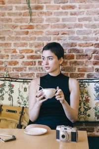 Woman with short hair holding coffee while sitting in cafe