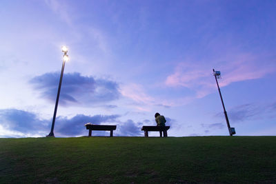 Low angle view of woman sitting on bench against sky at park