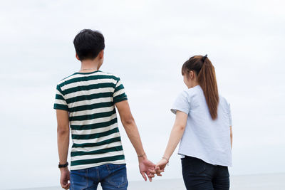 Rear view of couple holding hands against clear sky