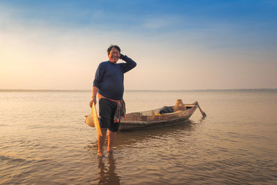 Man holding hat while standing in sea against sky