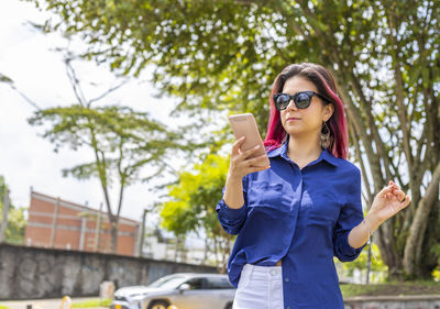 Young woman using phone while standing on tree