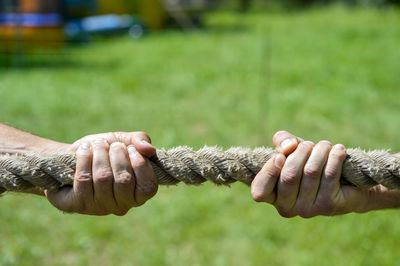 Close-up of hands holding rope on field