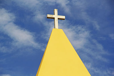 Low angle view of yellow cross against blue sky