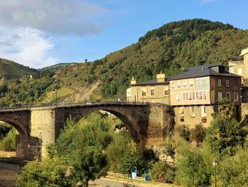 Arch bridge amidst trees and buildings against sky