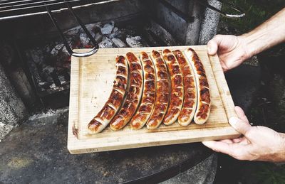 Cropped hand holding wooden board with grilled sausages by oven