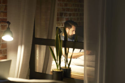 Rear view of woman looking through window at home