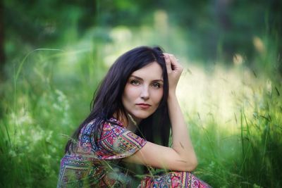 Beautiful woman looking away while sitting on grassy field at park