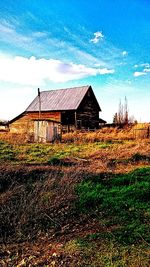 House on grassy field against cloudy sky