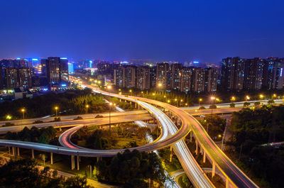 Illuminated modern highways against cityscape by night