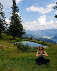 Portrait of young woman sitting on field against sky