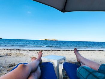 Low section of people on beach against clear blue sky