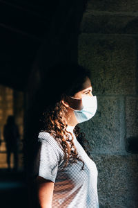 Side view of woman standing against window wearing face mask