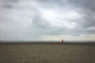 Man standing at beach against cloudy sky
